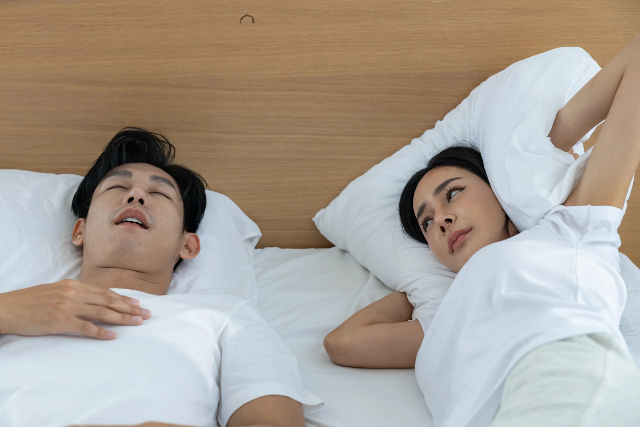 Woman covering her ears while her partner snores loudly beside her